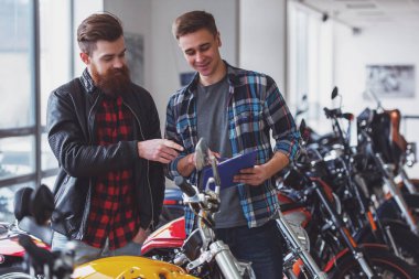 Yakışıklı genç sakallı adam siyah deri ceketli ve çekici sarışın adam konuşuyor ve motosiklet incelenirken gülümseyen