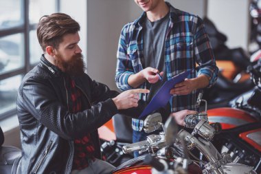 Yakışıklı genç sakallı adam siyah deri ceketli ve çekici sarışın adam konuşuyor ve motosiklet, kırpılmış incelenirken gülümseyen