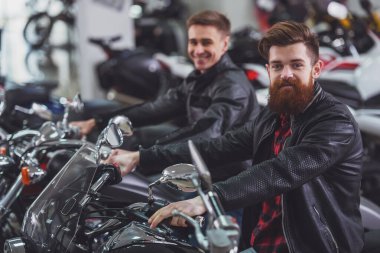 Siyah deri ceket yakışıklı genç sakallı ve sarışın adam kameraya bakarak ve motosiklet üzerinde otururken gülümseyen