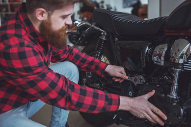 Yakışıklı genç sakallı adam rahat kıyafetler içinde bir motosiklet tamiri