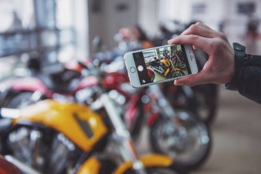 Siyah deri ceketli adamı bir motosiklet salonda duran bir akıllı telefon kullanarak fotoğraf yapıyor yakın çekim