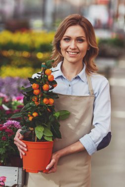 Güzel ve genç birbayan önlük ağaç bitki, turuncu holding, kameraya bakıyor ve duran orangery içinde gülümseyen