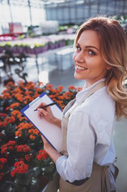 Güzel ve genç birbayan önlük bitkiler hakkında notlar, kameraya bakıyor ve duran orangery içinde gülümseyen