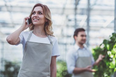 Güzel ve genç birbayan önlük cep telefonda konuşurken ve orangery içinde adam arka plan ayakta iken gülümseyen