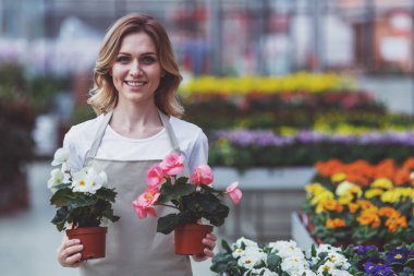 Güzel ve genç birbayan önlük bitkiler holding, kameraya bakıyor ve duran orangery içinde gülümseyen