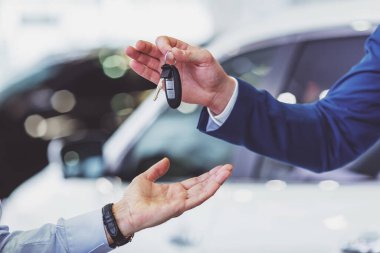 Yakışıklı delikanlı klasik mavi elbiseli bir Otomobil Fuarı olarak orta yaşlı müşteriye araba anahtarlarını veriyor