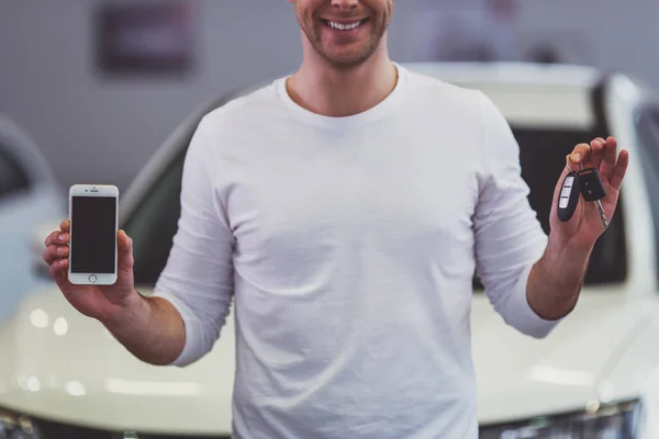 Guapo Joven Está Sonriendo Sosteniendo Las Llaves Teléfono Inteligente Mientras — Foto de Stock