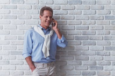 Yakışıklı orta yaşlı adam cep telefonunda gülümseyen ve uzak duran beyaz tuğla duvara bakarak konuşuyor