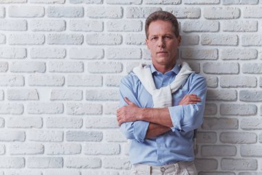 Yakışıklı orta yaşlı adam beyaz tuğla duvarın karşısında dururken kamera bakıyor