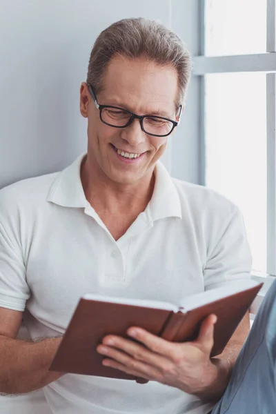 Guapo Hombre Mediana Edad Gafas Está Leyendo Sonriendo Mientras Está —  Fotos de Stock