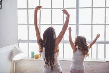 Arkadan görünüşü güzel genç anne ve onun sevimli küçük kızı sabah esneme ve germe