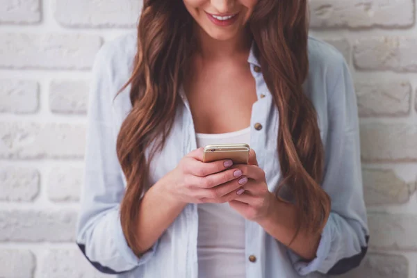 年轻漂亮的女人是使用智能手机 微笑着 墙上的白砖 — 图库照片