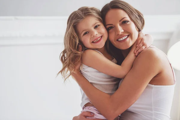 美しい若いお母さんと彼女の小さな娘が寄り添う カメラを見て 自宅のベッドの上に座ってながら笑顔 — ストック写真