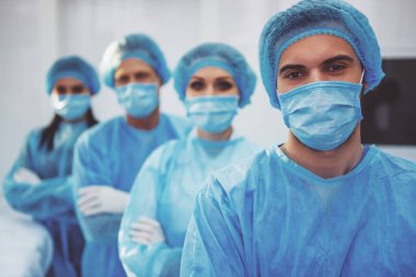 Güzel doktorlar kameraya bakıyor ve gülümsüyor, modern bir ameliyathane doğrultusunda ayakta