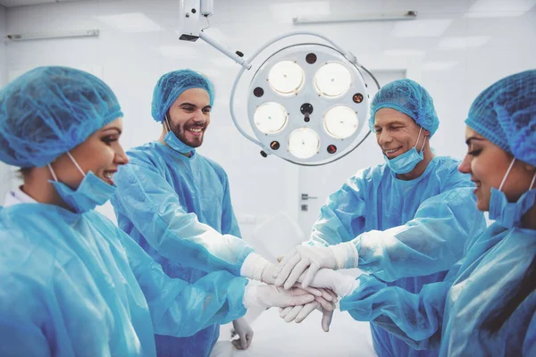 Zespół Chirurgów Łącząc Swoje Ręce Uśmiechnięty Stojąc Nowoczesnej Sali Operacyjnej — Zdjęcie stockowe