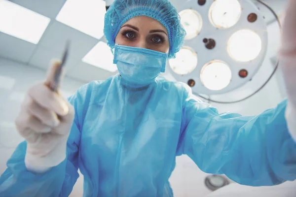 美丽的女外科医生拿着手术刀准备操作和看着相机 站在一个现代的手术室 底视图 — 图库照片
