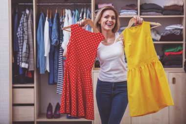 Güzel kız gülümseyerek ve soyunma odasina elbise seçerken kameraya bakıyor