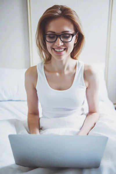 Piękna Blondynka Okularach Jest Pomocą Laptopa Uśmiechając Się Siedząc Łóżku — Zdjęcie stockowe