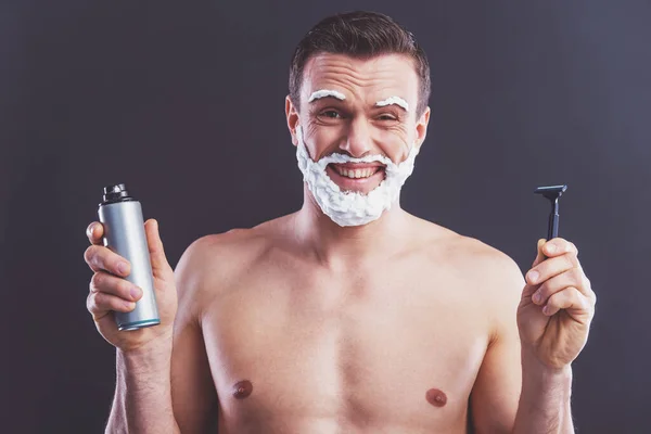 帅哥裸体的男人 他脸上剃须泡沫是微笑 剃须泡沫一瓶和一支刮胡刀 坚持一个黑暗的背景 — 图库照片