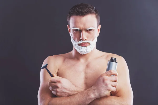 帅哥裸体的男人 他脸上剃须泡沫剃须泡沫一瓶和一支刮胡刀 坚持一个黑暗的背景 — 图库照片