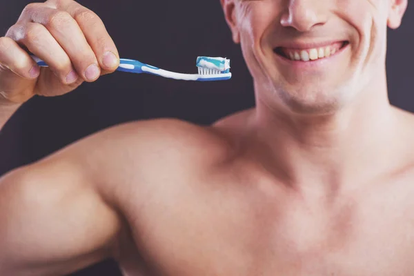 肖像的英俊裸体男子拿着一把牙刷和牙膏和微笑 在黑暗的背景下 — 图库照片
