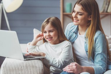 Güzel genç anne ve küçük kızı bir dizüstü bilgisayar kullanarak ve evde kanepede otururken gülümseyen