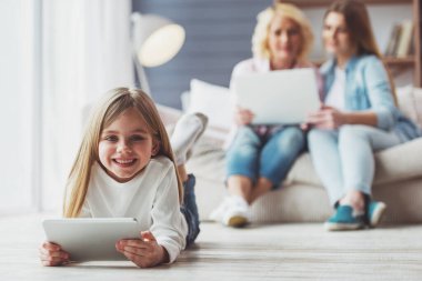 Küçük kız anne ve büyükanne evde kanepede otururken bir dizüstü bilgisayar kullanıyorsanız arka planda tablet, kullanma