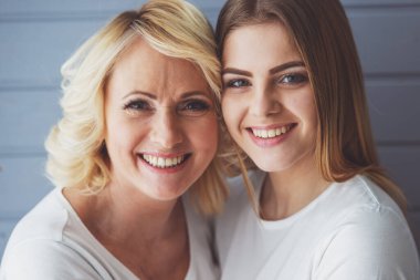 Güzel olgun anne ve kızı sarılma Portresi, kamera bakarak ve gülümseyerek, gri arka plan karşı