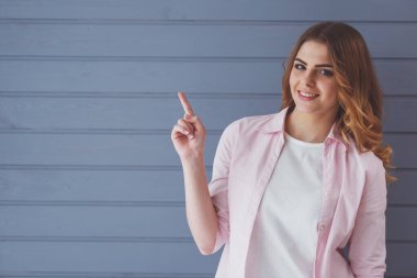 Güzel genç kadın kameraya bakıyor, işaret ediyor ve gülümsüyor, gri arka plana karşı duruyor