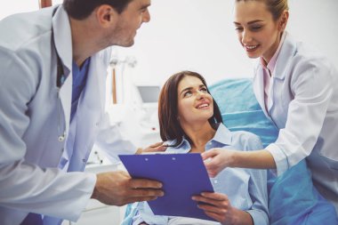 Güzel bayan hasta ve iki doktor klasörde belgelerle bakarak ve gülümseyen, doktor ofisinde
