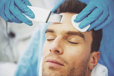 Alma yüz cilt bakımı, yakın çekim yakışıklı adam portresi. Doktor bir modern ekipman kullanarak yordamı taahhüt