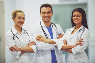 Üç güzel genç doktor kameraya bakıyor ve gülümseyerek,'hastane salonunda çapraz kolları olan ayakta