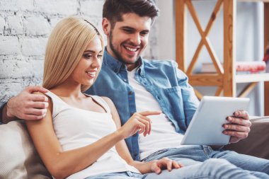 Güzel genç çift tablet, sarılma ve evde kanepede otururken gülümseyen kullanma