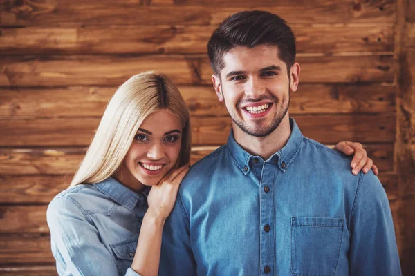 美丽的年轻夫妇 在牛仔裤的肖像衣服拥抱 看着相机和微笑 站在木墙 — 图库照片