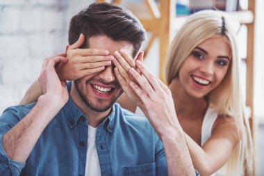 Güzel genç çift oynama ve evde kanepede otururken gülümseyerek. Kız erkek gözleri koruyor