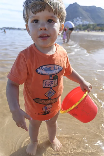 Malé dítě hraje na pláži s červeným kbelík — Stock fotografie
