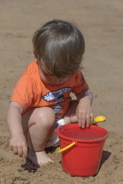 Niño jugando en la playa con cubo rojo —  Fotos de Stock