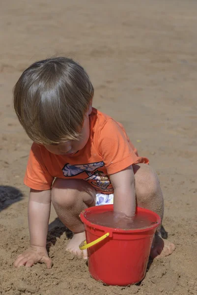 Niño jugando en la playa con cubo rojo —  Fotos de Stock