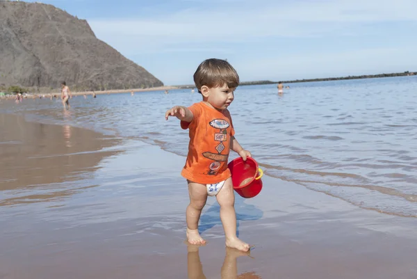 Malé dítě hraje na pláži s červeným kbelík — Stock fotografie