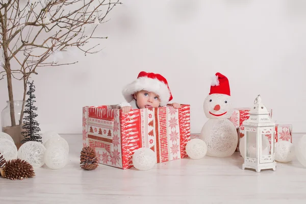 A young baby is staring at the camera wearing a Santa Christmas hat. Stock Photo