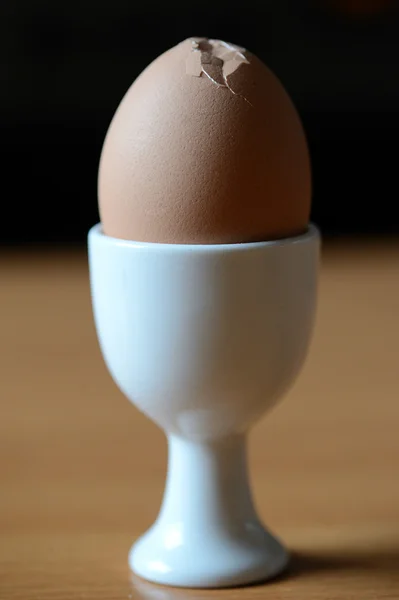 Коричневое яйцо в белой чашке на деревянном столе — стоковое фото