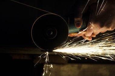 Öğütücüyle metal kesen bir işçi. Demir öğütürken kıvılcımlar