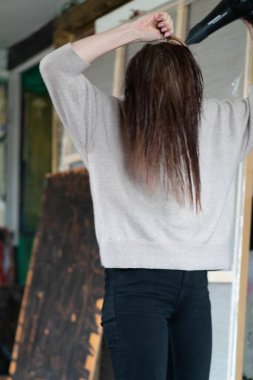 Genç ve güzel bir kadın saçını saç kurutma makinesiyle tarıyor.