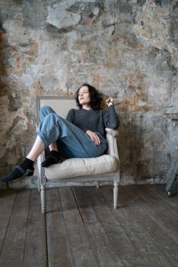 Stüdyoda genç ve güzel bir kadının portresi. Kot pantolonun içinde duruyor. Pencerenin yanında duruyor.