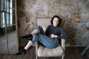 Stüdyoda genç ve güzel bir kadının portresi. Kot pantolonun içinde duruyor. Pencerenin yanında duruyor.