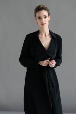 Genç ve güzel bir kadın stüdyoda siyah bir pelerinle poz veriyor.