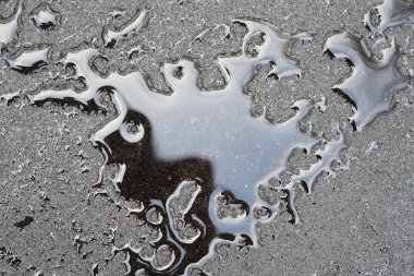 Siyah ıslak bir yolda su damlacıklarının dokusu, kenarlara sıçramış.