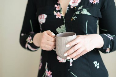 Genç bir kadın elinde bir kupayla stüdyoda duruyor.