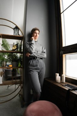 Genç ve güzel bir kadın pencerenin yanında bir kazakla dikiliyor.