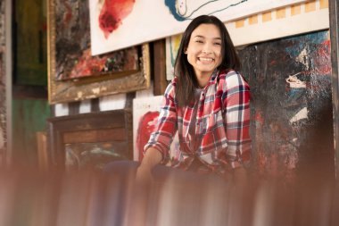 Stüdyoda kırmızı ekose gömlekli bir sandalyede oturan genç ve güzel bir kadın.